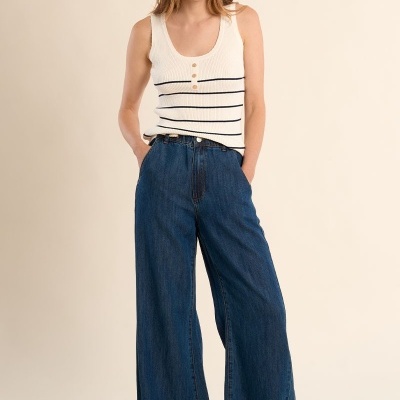 Modelo feminina com regata branca e calças de ganga largas azuis em fundo neutro