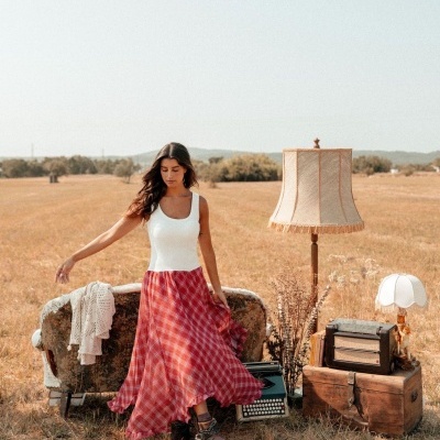 Mulher em vestido branco e saia vermelha junto a mobiliário vintage num campo