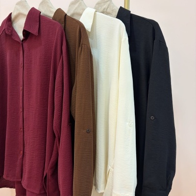 Quatro camisas femininas texturizadas nas cores vinho, castanho, branco e preto penduradas em cabides.