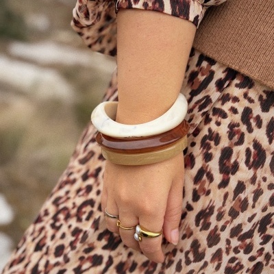 Pulso com pulseiras em resina bege e castanho e anéis, junto a vestido com padrão animal print castanho.