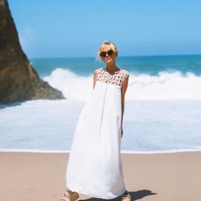 Mulher na praia a usar vestido branco longo com parte superior em padrão recortado e sandálias de cunha