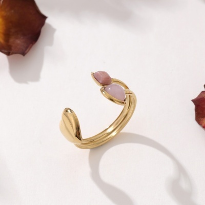 Anel dourado com pedras rosa em fundo branco com pétalas secas