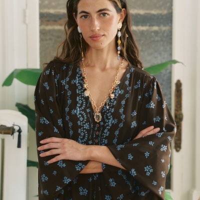 Mulher com vestido castanho de flores azuis e colar dourado com brincos longos