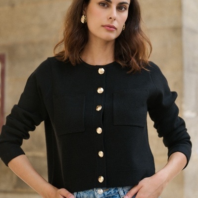 Mulher com camisola preta de malha com botões dourados e jeans azuis