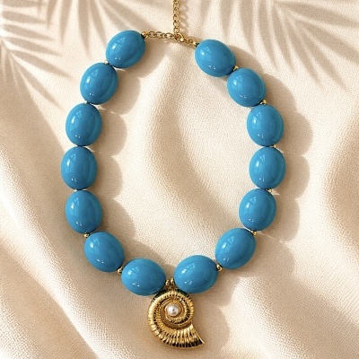 Colar azul com pendente dourado em forma de espiral e pérola sobre tecido bege