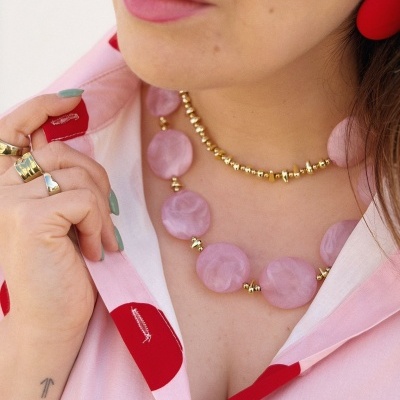 Colar rosa com contas grandes e pequenas douradas, brincos vermelhos e camisa rosa com bolinhas vermelhas