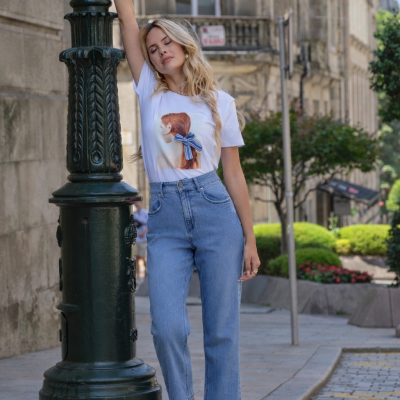 Modelo com t-shirt branca estampada, jeans azuis e sandálias pretas em rua urbana