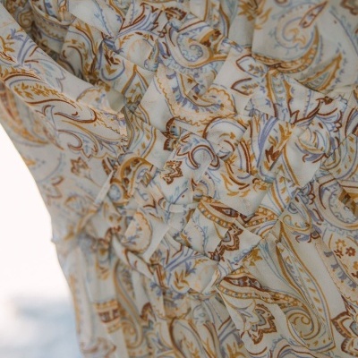 Tecido de vestido com padrão paisley em azul, castanho e amarelo sobre creme com pregas.