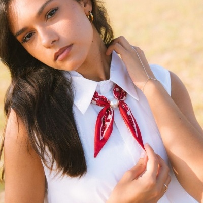 Colar prateado com pérola sobre camisa branca e lenço vermelho.