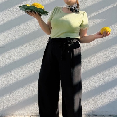Mulher vestida com blusa verde, calças pretas e sapatilhas brancas segurando limões num prato verde