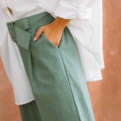 Calças verdes com bolso e cinto, camisa branca com botões dourados.