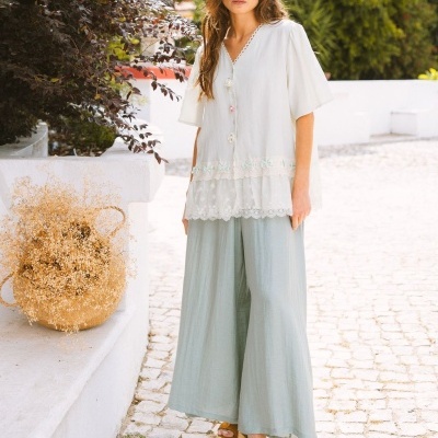 Conjunto feminino com blusa branca e calças largas verde claro, sandálias castanhas e ambiente exterior.