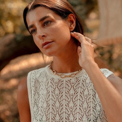 Mulher com colar dourado e top branco rendado em ambiente natural