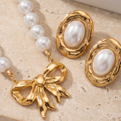 Colar e brincos com pérolas falsas e metal dourado sobre superfície clara.