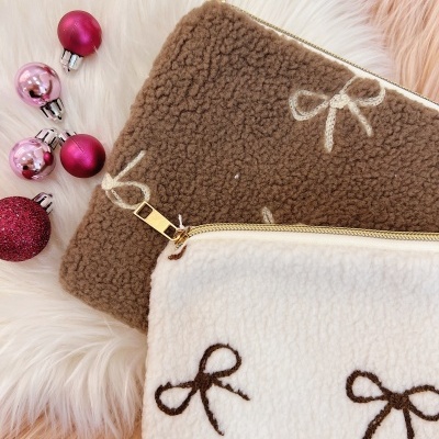 Duas bolsas felpudas castanha e creme com laços bordados e fechos dourados