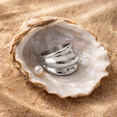 anel prateado dentro de uma concha na areia com pérola