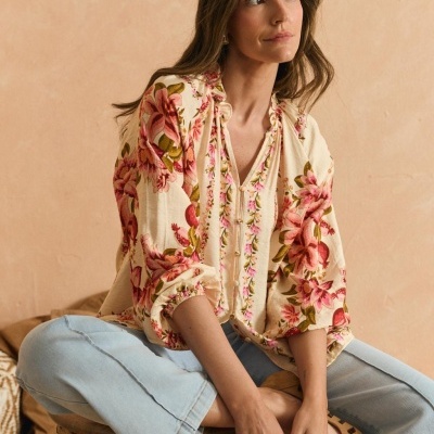 Blusa feminina creme com flores rosa sentada com calças de ganga azul claro