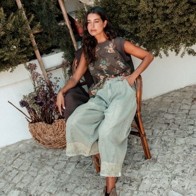 Mulher sentada com calças largas verdes claras e top floral num ambiente exterior com piso de calçada portuguesa
