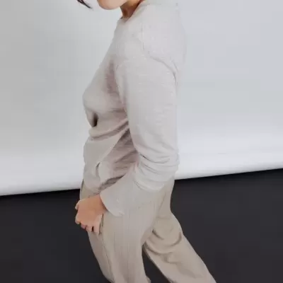 Mulher a usar camisola cinza claro e calças largas bege em fundo neutro.