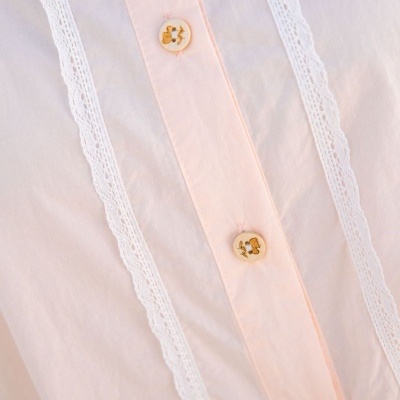 Peça de roupa rosa claro com renda branca e botões bege com detalhes dourados
