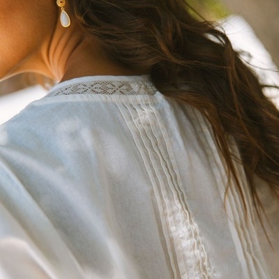 Blusa branca feminina com renda e pregas usada por mulher com brincos dourados.