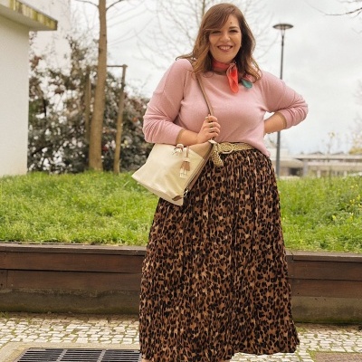 Mulher vestida com blusão rosa, saia animal print e sandálias castanhas ao ar livre