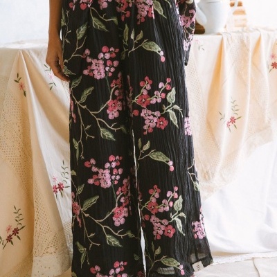 Calças largas pretas com padrão floral rosa e folhas verdes em ambiente interior