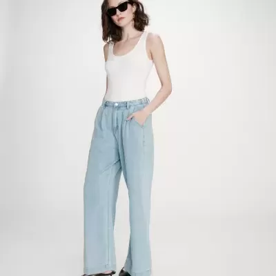 Mulher com top branco, calças largas de ganga azul clara e sapatos pretos, óculos de sol