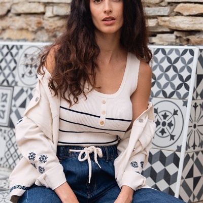 Mulher com roupa casual em ambiente exterior com parede de pedra e bancos com azulejos