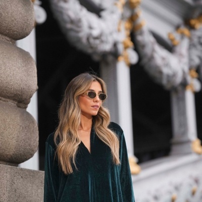 Mulher com vestido verde escuro aveludado e óculos de sol com armação dourada