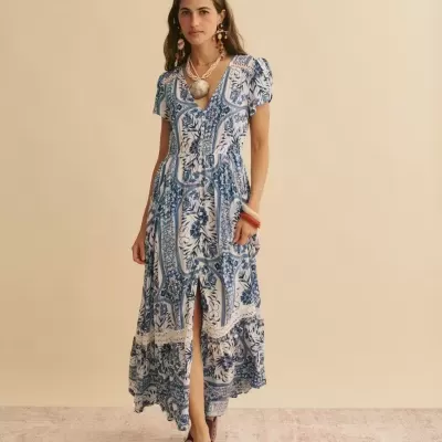 Vestido azul e branco com padrão floral e folhos, usado por mulher com acessórios grandes e sandálias castanhas.