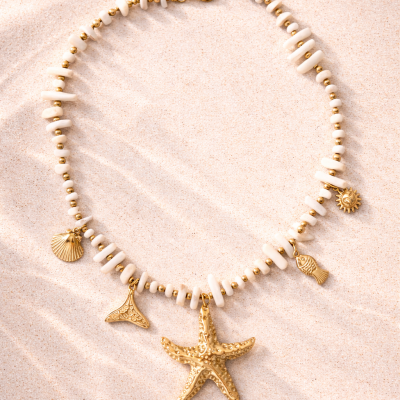 Colar branco com pendentes dourados marinhos sobre areia