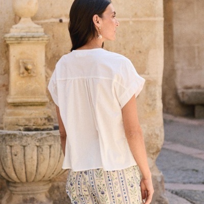 Mulher vista de costas com t-shirt branca e calças florais em ambiente exterior antigo
