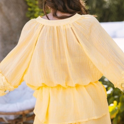Blusa amarela de tecido leve com detalhes em renda vista de costas ao ar livre