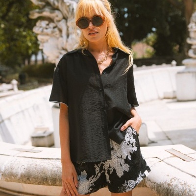 Mulher com camisa preta e calções com padrão floral branco ao ar livre