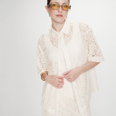 Blusa feminina creme de renda com padrão floral e óculos de sol com lentes amarelas.