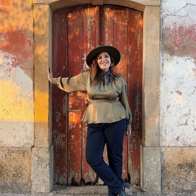 Mulher em roupa verde e preta em frente a porta vermelha em parede envelhecida