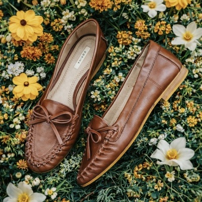 Mocassins castanhos em pele com laço frontal sobre flores coloridas