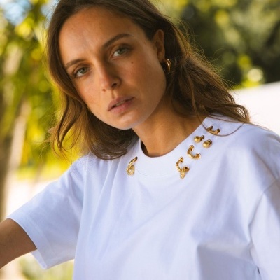 T-shirt branca com aplicações douradas em argolas junto ao decote usada por mulher