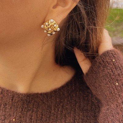 Brinco dourado com pérolas usado por pessoa com pulôver castanho