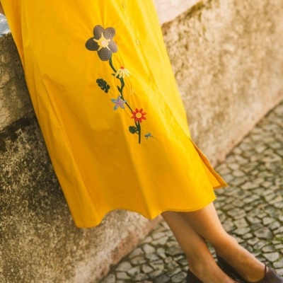 Vestido amarelo com bordado floral e sapatos castanhos num piso de calçada