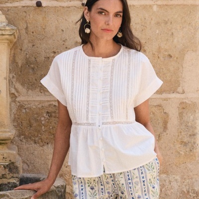 Mulher com blusa branca de manga curta e calças florais perto de parede de pedra