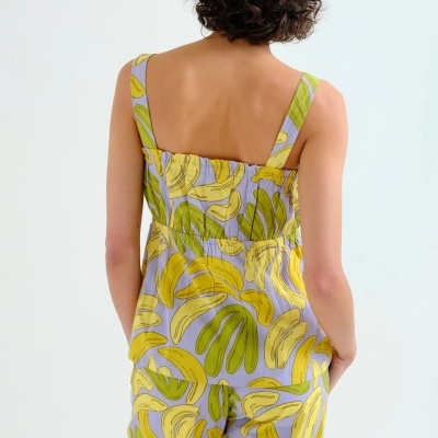 Conjunto de pijama feminino de bananas amarelas e verdes em fundo lilás visto das costas.