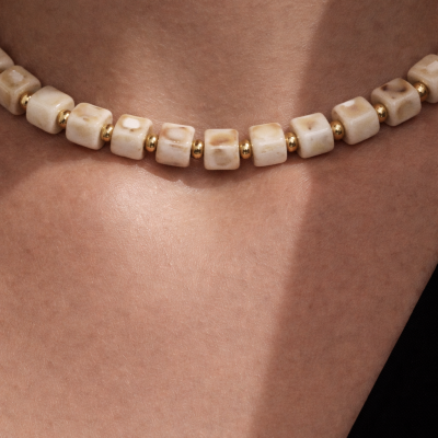 Colar com contas cuboides bege e esferas douradas ao redor do pescoço