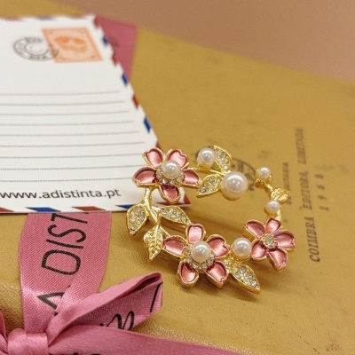 Anel dourado com flores cor de rosa, pérolas e folhas com cristais sobre caixa amarela e laço rosa