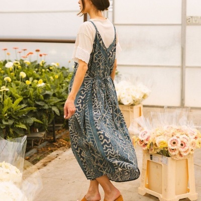 Mulher de vestido azul com padrão geométrico e t-shirt branca em estufa com flores.