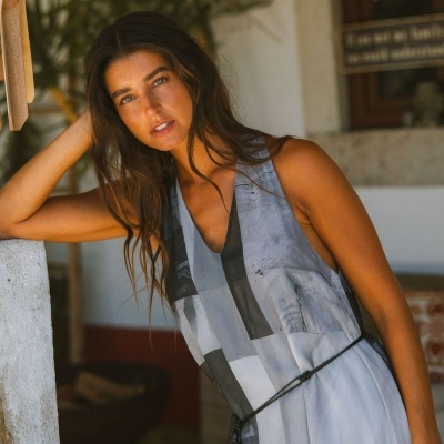 Mulher com vestido longo cinza e preto com padrão geométrico, cinto preto e cabelo castanho
