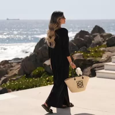 Mulher de vestido preto e bolsa de palha junto ao mar
