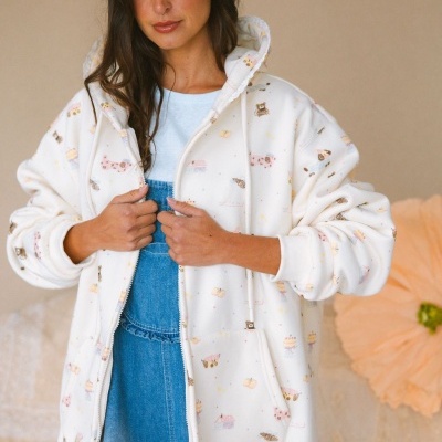 Casaco branco com padrão de desenhos coloridos e capuz, usado por mulher em fundo neutro