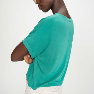 Pessoa com t-shirt verde água e calças brancas de perfil